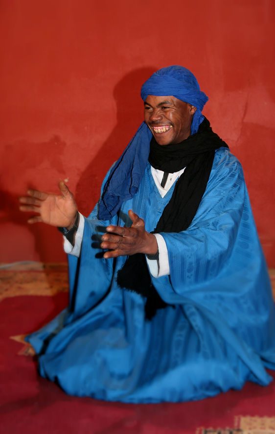Performer in a blue robe and turban clapping at Chez Ali