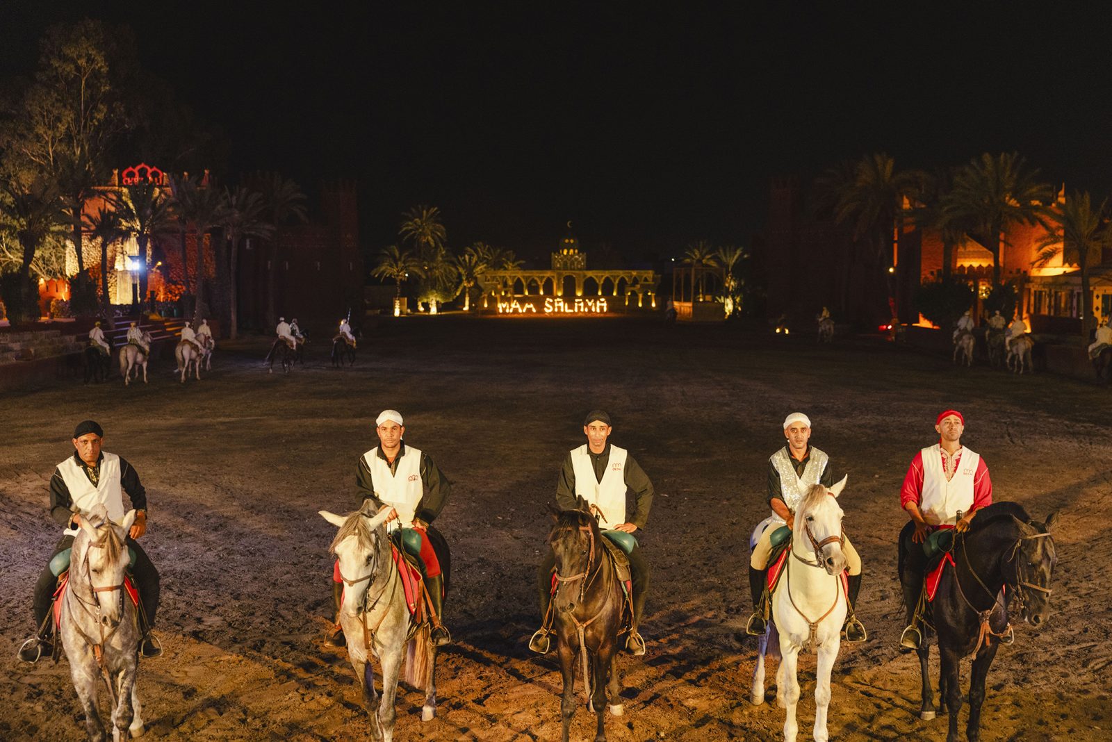 Cavaliers de la Fantasia alignés en blanc dans l'arène la nuit à Chez Ali