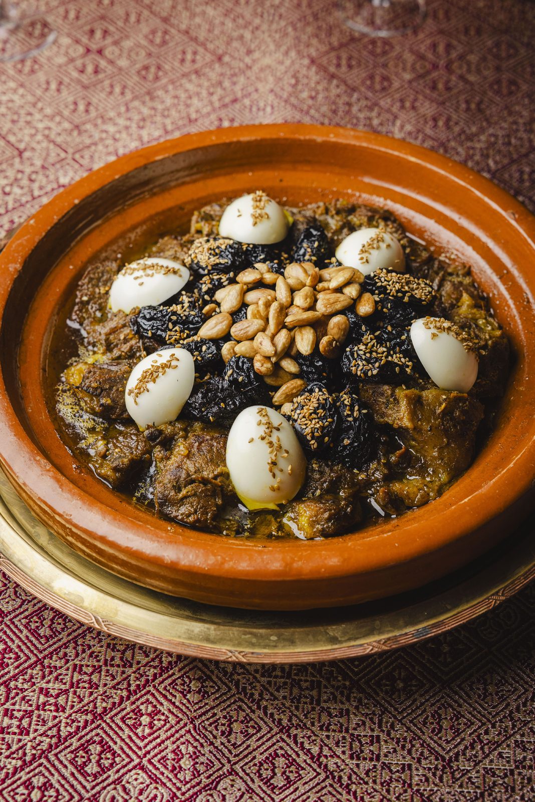 Beef tagine with prunes, eggs and almonds on a patterned tablecloth at Chez Ali