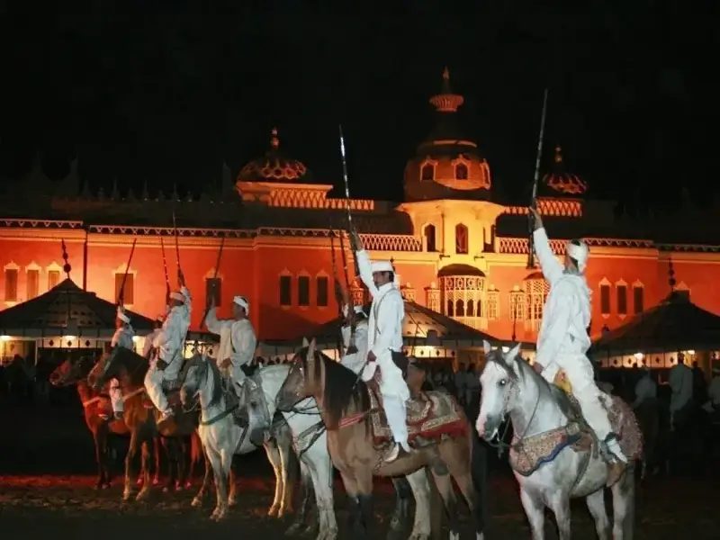 Horsemen with raised rifles in front of the illuminated palace at Chez Ali